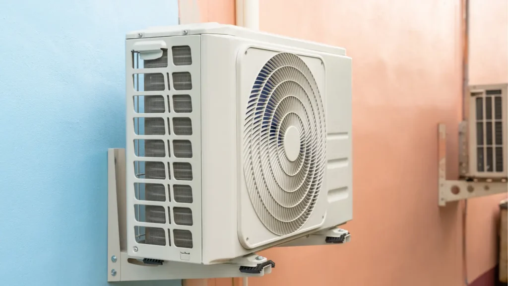 A white outdoor air conditioning unit, part of an HVAC Repair and Installation setup, is mounted on a blue wall, with another unit in the background fixed to a peach-colored wall.