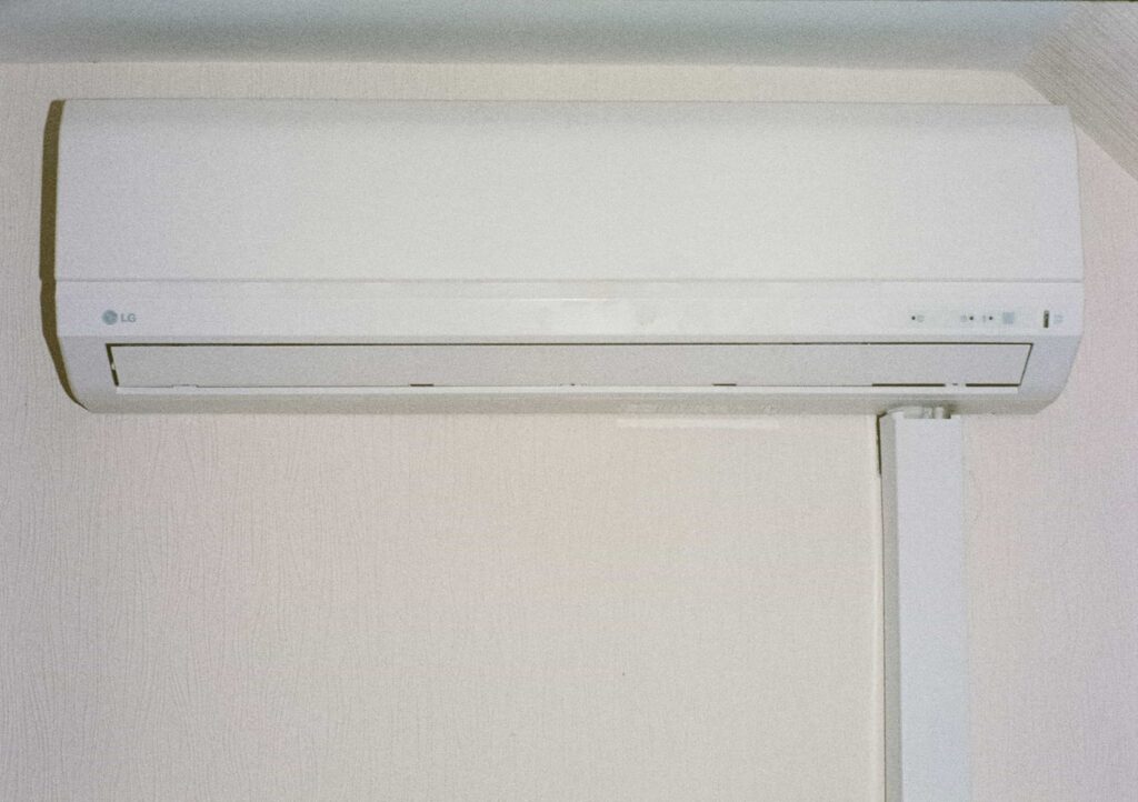 Wall-mounted white air conditioning unit with a vent at the bottom, installed on a light-colored wall.