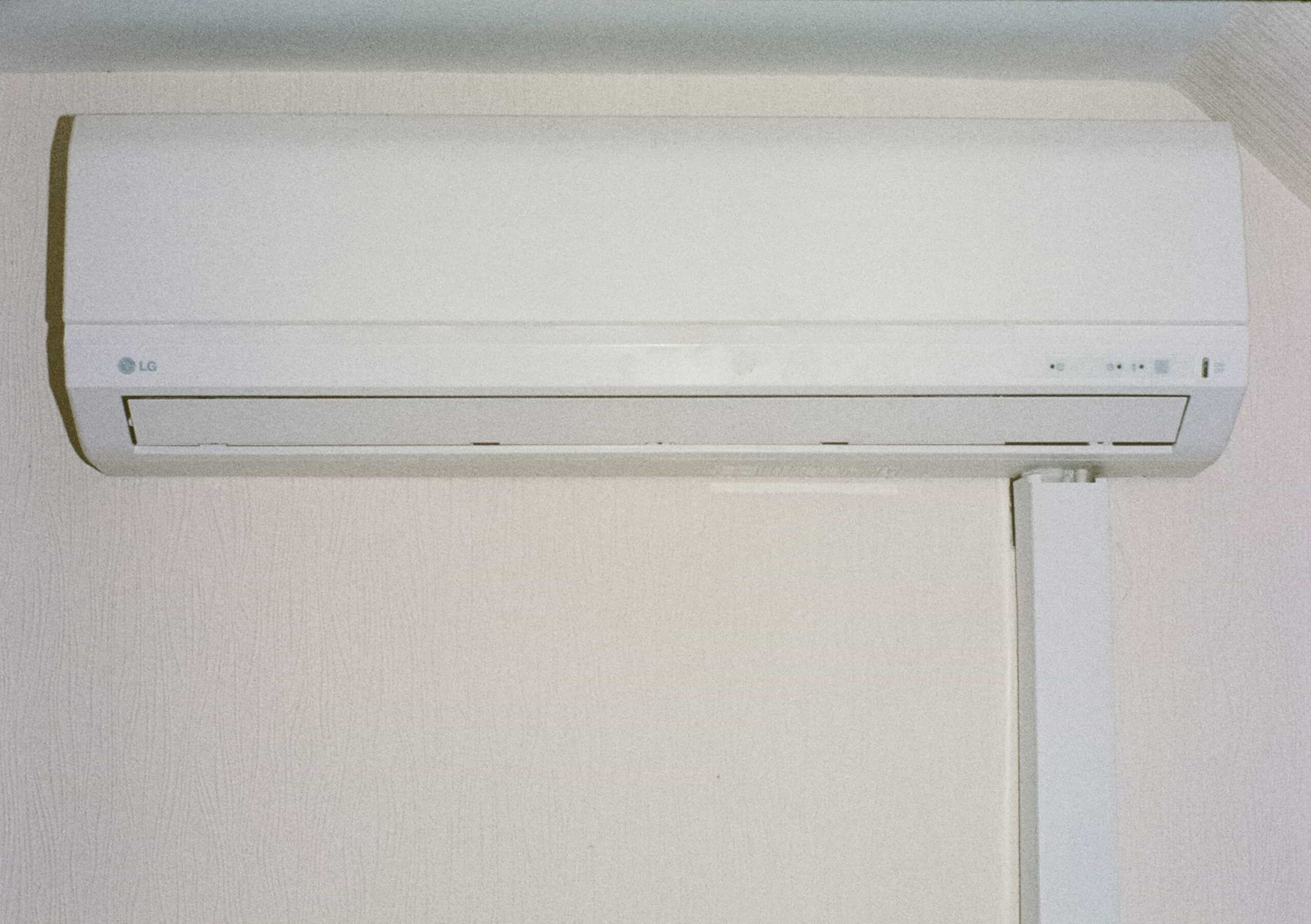 Wall-mounted white air conditioning unit with a vent at the bottom, installed on a light-colored wall.